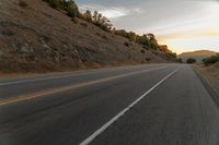 a highway stretches off a hill to the horizon at sunset, with a lone cyclist and some hills in the distance