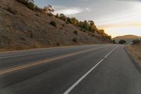 a highway stretches off a hill to the horizon at sunset, with a lone cyclist and some hills in the distance