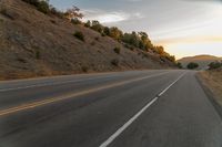 a highway stretches off a hill to the horizon at sunset, with a lone cyclist and some hills in the distance