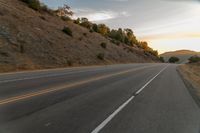 a highway stretches off a hill to the horizon at sunset, with a lone cyclist and some hills in the distance