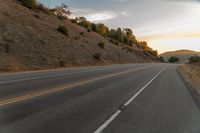 a highway stretches off a hill to the horizon at sunset, with a lone cyclist and some hills in the distance