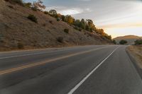 a highway stretches off a hill to the horizon at sunset, with a lone cyclist and some hills in the distance