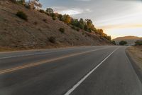 a highway stretches off a hill to the horizon at sunset, with a lone cyclist and some hills in the distance