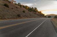 a highway stretches off a hill to the horizon at sunset, with a lone cyclist and some hills in the distance