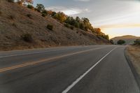 a highway stretches off a hill to the horizon at sunset, with a lone cyclist and some hills in the distance