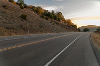 a highway stretches off a hill to the horizon at sunset, with a lone cyclist and some hills in the distance