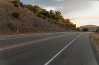 a highway stretches off a hill to the horizon at sunset, with a lone cyclist and some hills in the distance