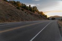 a highway stretches off a hill to the horizon at sunset, with a lone cyclist and some hills in the distance