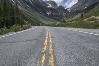 a yellow strip is marking the middle of a road, with snow covered mountains in the distance