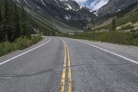 a yellow strip is marking the middle of a road, with snow covered mountains in the distance