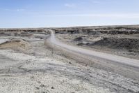 a dirt road is surrounded by some hills and desert like terrain as the vehicle sits on it