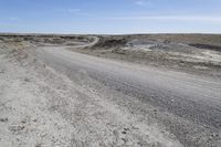 a dirt road is surrounded by some hills and desert like terrain as the vehicle sits on it