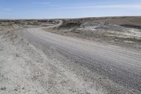 a dirt road is surrounded by some hills and desert like terrain as the vehicle sits on it