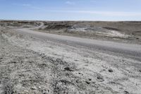 a dirt road is surrounded by some hills and desert like terrain as the vehicle sits on it