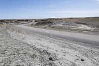 a dirt road is surrounded by some hills and desert like terrain as the vehicle sits on it