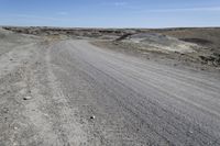 a dirt road is surrounded by some hills and desert like terrain as the vehicle sits on it