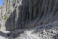 people walking through a rocky canyon below a waterfall, with the mountains to the side