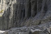 people walking through a rocky canyon below a waterfall, with the mountains to the side