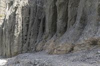 people walking through a rocky canyon below a waterfall, with the mountains to the side