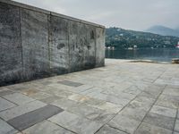 a stone walkway with a bench on a side walk next to water and mountain backdrop