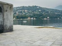 a stone walkway with a bench on a side walk next to water and mountain backdrop