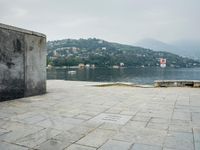 a stone walkway with a bench on a side walk next to water and mountain backdrop