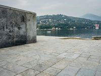 a stone walkway with a bench on a side walk next to water and mountain backdrop