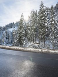 snow on the mountains surrounding an empty highway, trees and sky in the background,