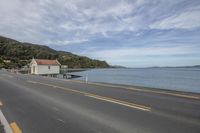 there is a road with houses beside the water and mountains in the distance behind the road