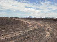 an animal walks across a large dirt and gravel plain in the desert, with mountains in the background