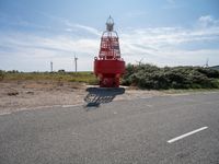 a red lighthouse sits on top of the street next to the road with windmills in the background