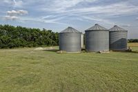 two large grain bins sit in the center of a field, surrounded by silos