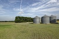 two large grain bins sit in the center of a field, surrounded by silos