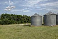 two large grain bins sit in the center of a field, surrounded by silos