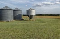 two large grain bins sit in the center of a field, surrounded by silos