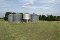two large grain bins sit in the center of a field, surrounded by silos