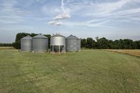 two large grain bins sit in the center of a field, surrounded by silos