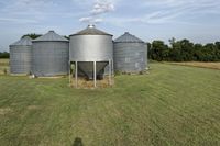 two large grain bins sit in the center of a field, surrounded by silos