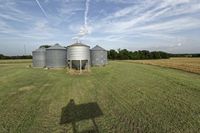 two large grain bins sit in the center of a field, surrounded by silos