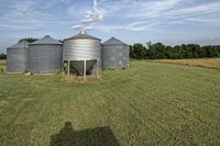 two large grain bins sit in the center of a field, surrounded by silos