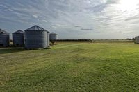 two large grain bins sit in the center of a field, surrounded by silos