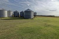 two large grain bins sit in the center of a field, surrounded by silos