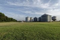 two large grain bins sit in the center of a field, surrounded by silos