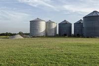 two large grain bins sit in the center of a field, surrounded by silos