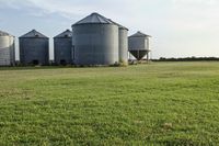 two large grain bins sit in the center of a field, surrounded by silos