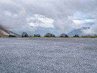 a black motorcycle parked in an empty area with mountains in the background, including snow and clouds