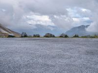 a black motorcycle parked in an empty area with mountains in the background, including snow and clouds