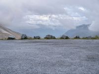 a black motorcycle parked in an empty area with mountains in the background, including snow and clouds