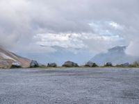 a black motorcycle parked in an empty area with mountains in the background, including snow and clouds