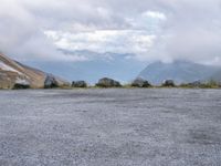 a black motorcycle parked in an empty area with mountains in the background, including snow and clouds